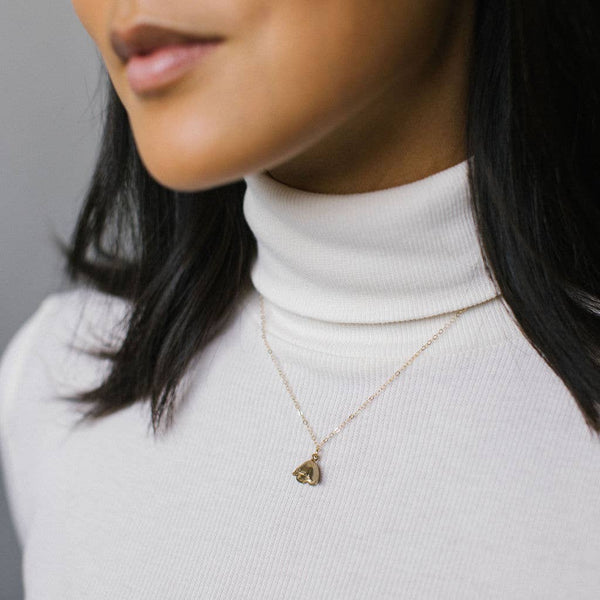 Woman wearing a white turtleneck and a necklace with a yellow bronze bell flower charm pendant.