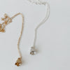 Two bell flower charm necklaces, one gold and one silver, on a light gray background