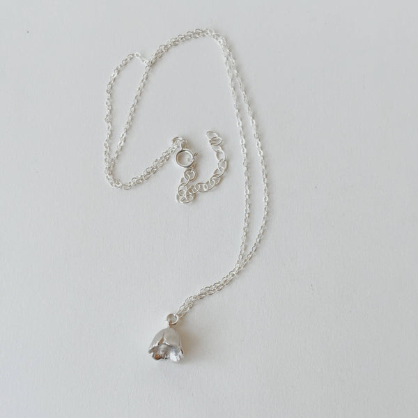 Silver necklace with a bell flower charm pendant on a light gray background