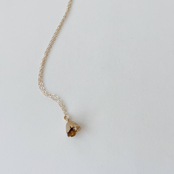 Gold necklace with a small yellow bronze bell flower pendant on a light gray background