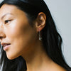 Close-up of a woman wearing a silver sparrow charm earring with a plain background