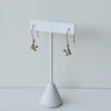 Yellow bronze sparrow charm earrings on a white earring stand against a light gray background