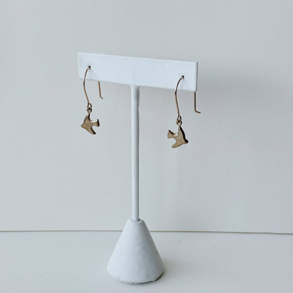 Yellow bronze sparrow charm earrings on a white earring stand against a light gray background