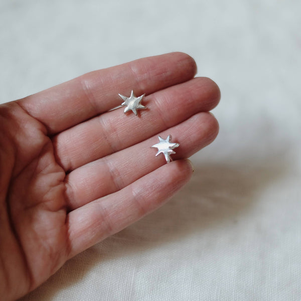 Small star-shaped earrings held in a hand against a plain background
