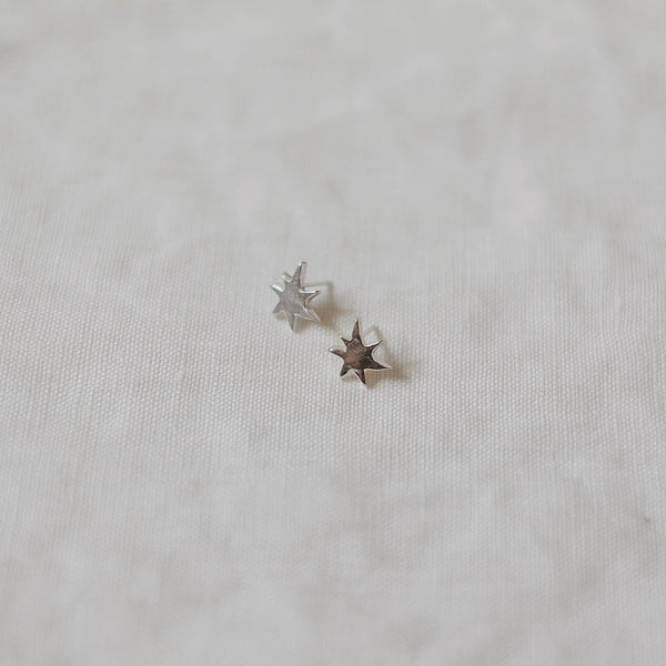 Two small sunburst silver earrings on a light fabric background
