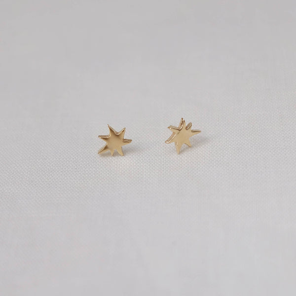 Yellow bronze star-shaped earrings on a light gray background