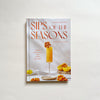 'Sips of the Season' cocktail recipe book by Sarah Gualtieri on a neutral background.