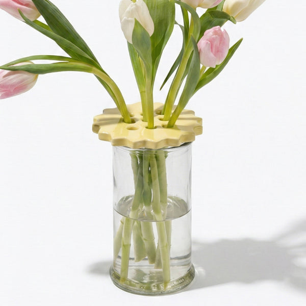 Clear glass vase with yellow ceramic flower frog holding pink and white tulips on a white background