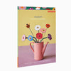 Product packaging with a pink watering can and colorful flowers on a yellow background