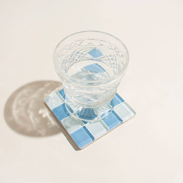 Clear glass with water on a blue mosaic coaster on a light beige surface