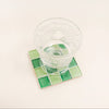 Clear glass on a green square coaster with a white background