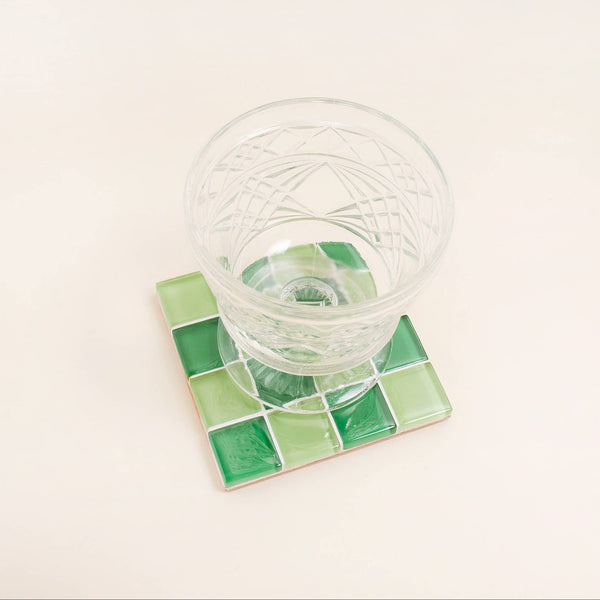 Clear glass on a green square coaster with a white background
