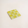 Square glass tile with two toned yellow checkered pattern on a beige background