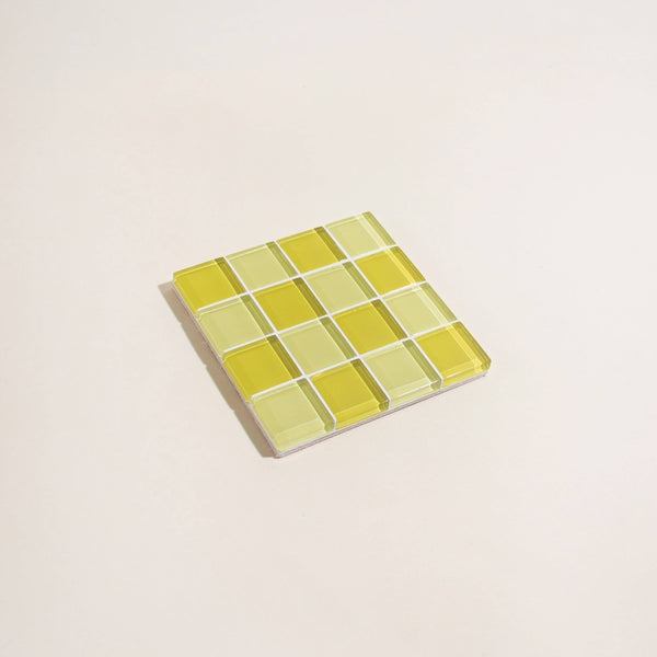 Square glass tile with two toned yellow checkered pattern on a beige background