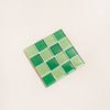 Square glass tile with green square pattern on a beige background