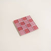 Square tile coaster with pink and red square pattern on a beige background