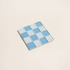 Square glass tile with blue checkered pattern on a beige background