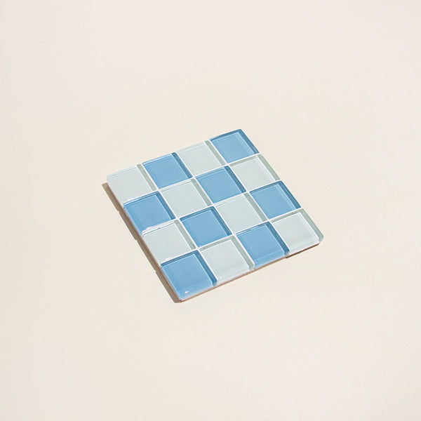 Square glass tile with blue checkered pattern on a beige background