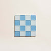 Grid of blue and clear glass tile coaster on a beige background