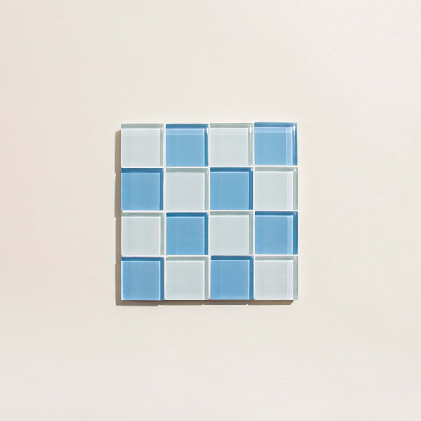 Grid of blue and clear glass tile coaster on a beige background