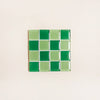Square tile with green and light green checkered pattern on a beige background