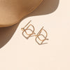 Gold earrings on a beige surface on an neutral background.