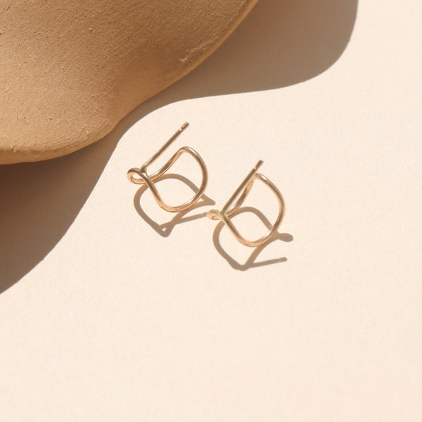 Gold earrings on a beige surface on an neutral background.