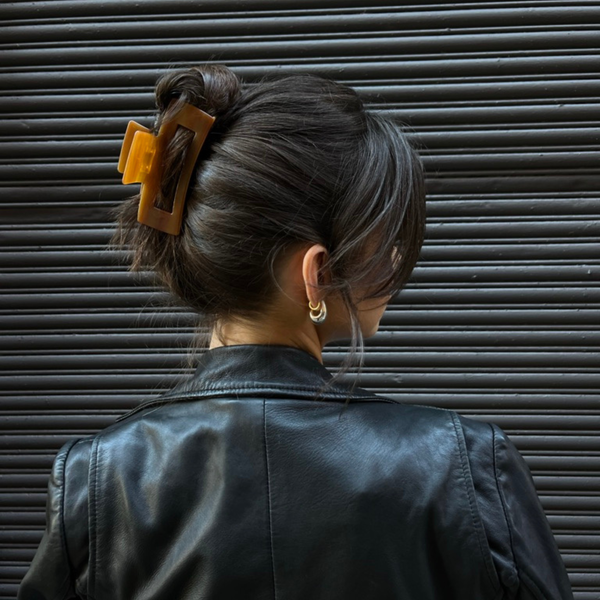 Person with a honey colored hair clip in their bun against a dark background