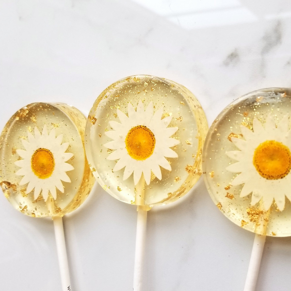 Three lollipops with daisy flowers embedded in them on a white background