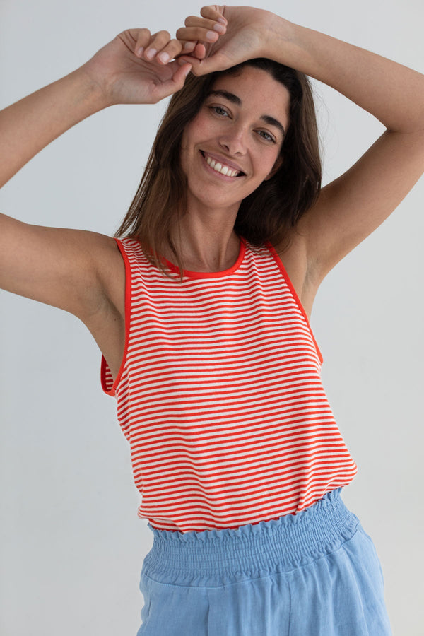 Woman wearing a red and white striped tank top and blue pants against a plain background