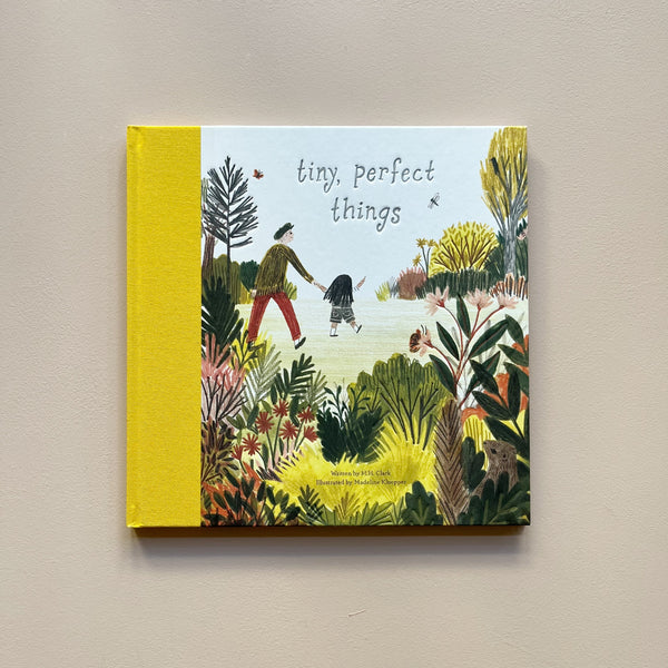 An illustrated children's book called 'Tiny, Perfect Things' with a cover design showing a parent and child walking through a bountiful nature area. The book sits against a neutral backdrop.