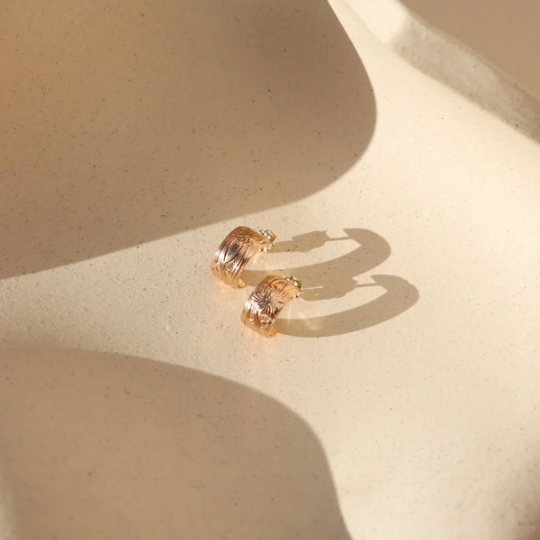 Pair of gold hoop earrings on a beige surface with soft shadows