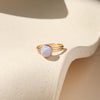 Gold ring with a light blue stone on a beige surface