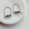 Pair of gold arch earrings with dalmation jasper cylindrical beads on a white background.
