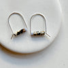 Pair of silver arch earrings with cylindrical beads on a white plate