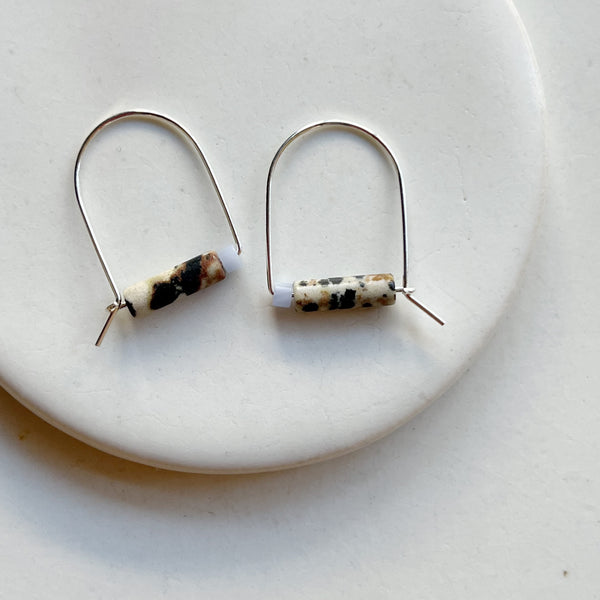 Pair of silver arch earrings with cylindrical beads on a white plate