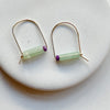 Gold arch earrings with green stone and purple bead on a white background.
