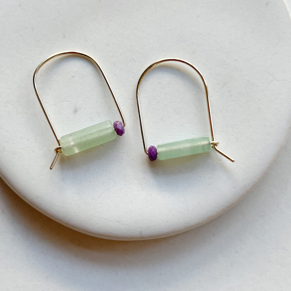 Gold arch earrings with green stone and purple bead on a white background.