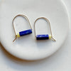 Pair of gold earrings with blue and yellow cylindrical beads on a white plate
