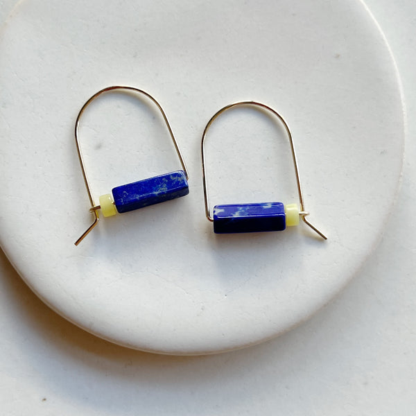 Pair of gold earrings with blue and yellow cylindrical beads on a white plate