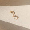 Pair of gold and opal huggie earrings on neutral background.