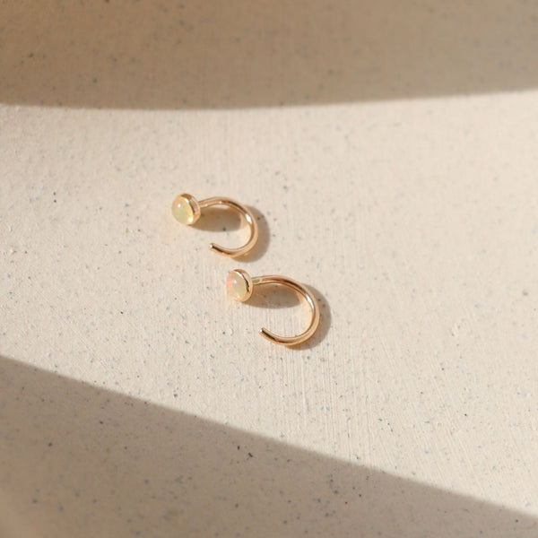 Pair of gold and opal huggie earrings on neutral background.