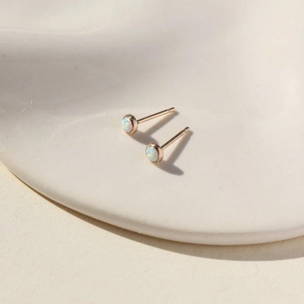 Gold opal stud earrings on neutral background.