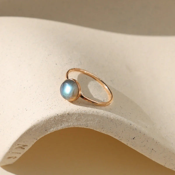 Gold ring with labradorite stone on neutral background.