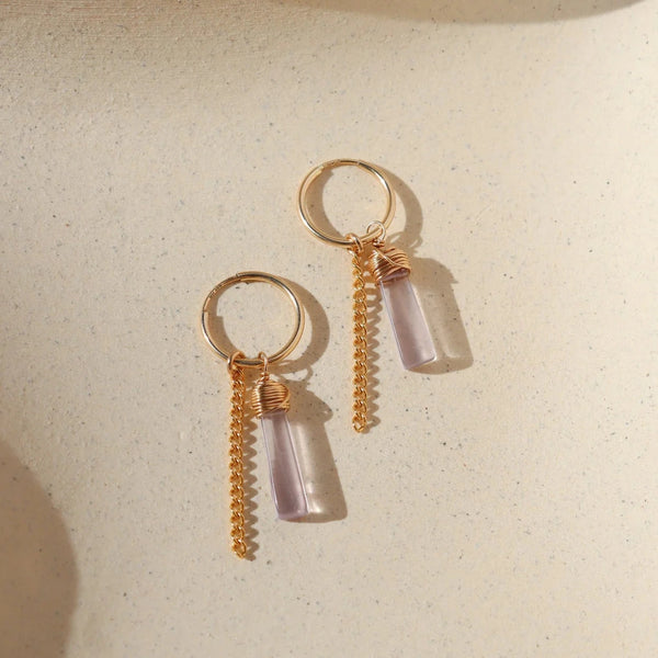 Gold hoop earrings with amethyst stone and gold chain drop on neutral background.