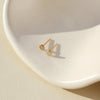 Gold stud earrings on a white dish with a beige background