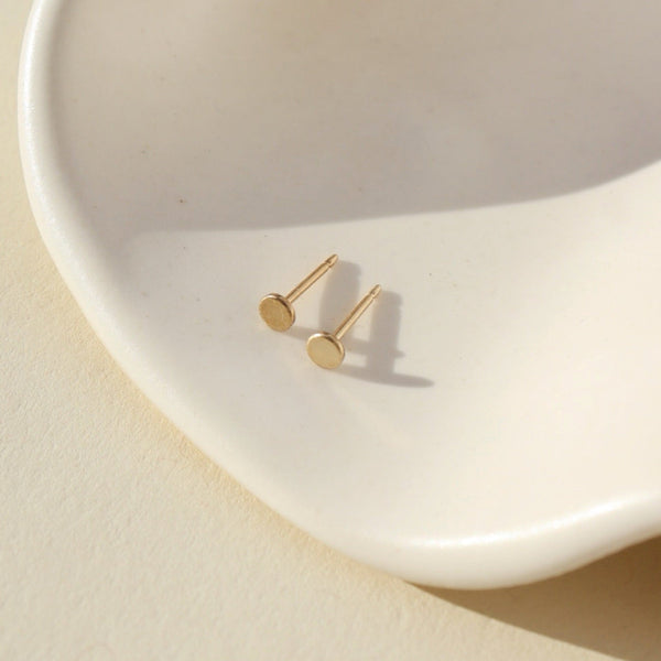 Gold stud earrings on a white dish with a beige background