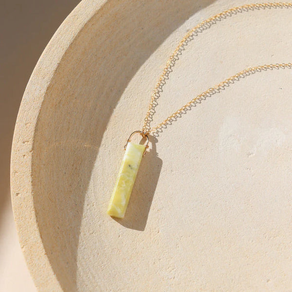 Delicate gold chain necklace with light green serpentine pendant on neutral background.