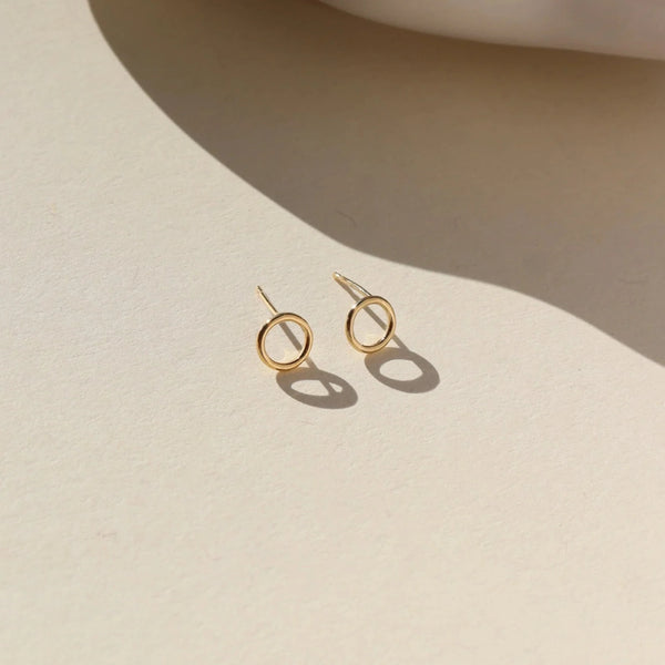 Gold mini circular stud earrings on a neutral background.