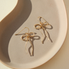 Gold bow-shaped earrings on a beige plate